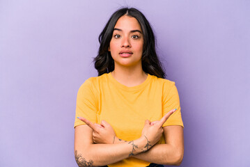 Obraz premium Young hispanic woman isolated on purple background points sideways, is trying to choose between two options.