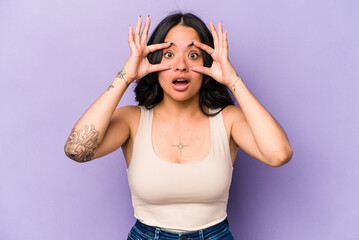 Young hispanic woman isolated on purple background keeping eyes opened to find a success opportunity.