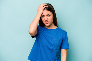 Young caucasian woman isolated on blue background forgetting something, slapping forehead with palm...