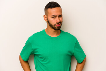 Young hispanic man isolated on white background frowning face in displeasure, keeps arms folded.