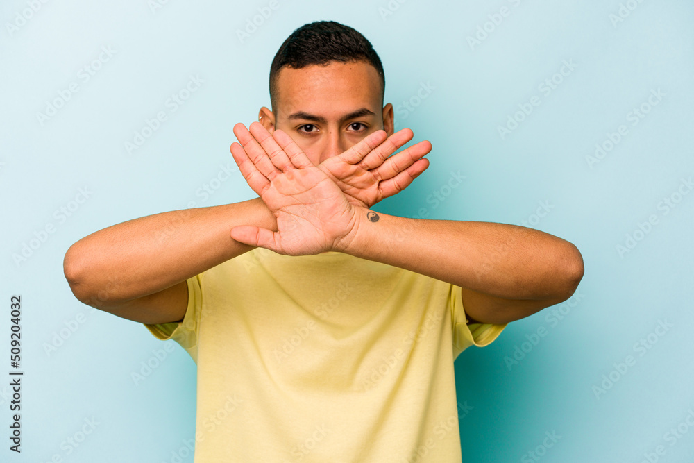 Wall mural young hispanic man isolated on blue background doing a denial gesture