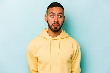 Young hispanic man isolated on blue background confused, feels doubtful and unsure.