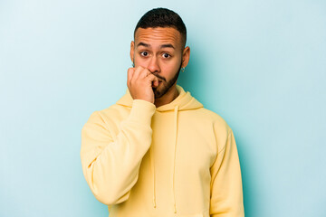 Young hispanic man isolated on blue background biting fingernails, nervous and very anxious.