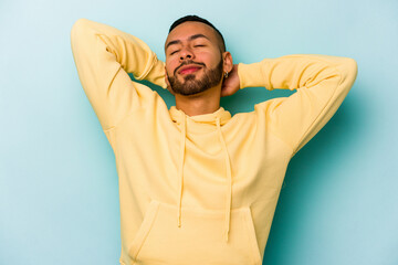 Young hispanic man isolated on blue background feeling confident, with hands behind the head.