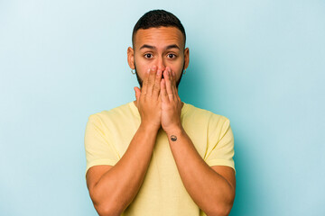 Young hispanic man isolated on blue background shocked, covering mouth with hands, anxious to discover something new.