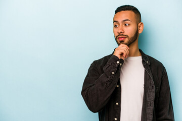 Young hispanic man isolated on blue background looking sideways with doubtful and skeptical...