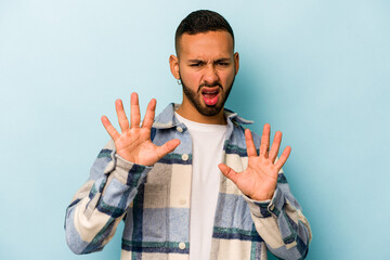 Young hispanic man isolated on blue background rejecting someone showing a gesture of disgust.
