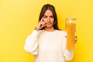 Young hispanic woman holding a spaghetti jar isolated on yellow background pointing temple with finger, thinking, focused on a task.