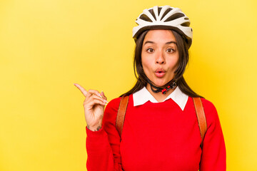 Young student hispanic woman wearing a bike helmet isolated on yellow background pointing to the side