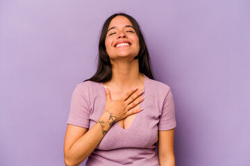 Young hispanic woman isolated on purple background laughs out loudly keeping hand on chest.