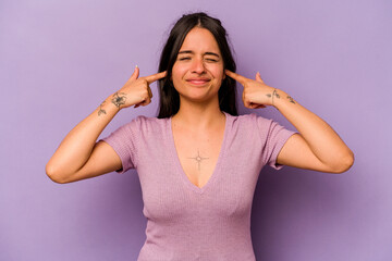 Young hispanic woman isolated on purple background covering ears with fingers, stressed and desperate by a loudly ambient.