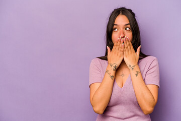 Young hispanic woman isolated on purple background thoughtful looking to a copy space covering mouth with hand.