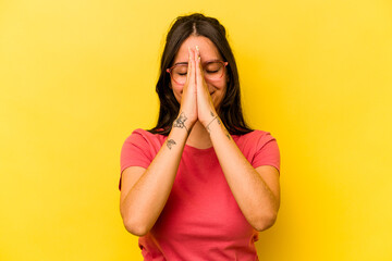 Young hispanic woman isolated on yellow background holding hands in pray near mouth, feels...