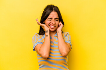 Young hispanic woman isolated on yellow background covering ears with hands.