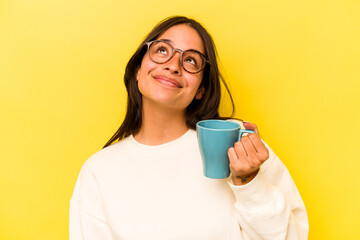Young hispanic woman holding a mug isolated on yellow background