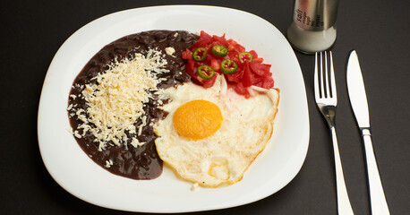 Fried egg accompanied with tomato and sliced jalapeño pepper, beans with grated cheese