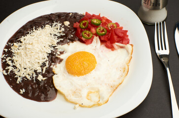 Fried egg accompanied with tomato and sliced jalapeño pepper, beans with grated cheese
