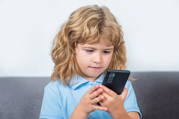 Fototapeta premium Little boy using smartphone, looking at screen, child holding phone in hands, playing mobile device game, watching cartoons online. Boy communicates on Internet. Child gadget addiction, insomnia
