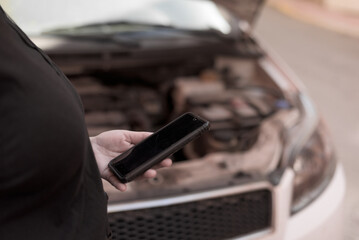 Woman's hand holding a mobile phone waiting for a call because her car has broken down.