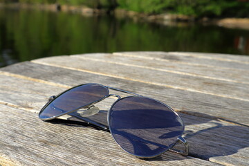 Fototapeta na wymiar Sunglasses next to a calm lake. Sunny day outside. Close up and isolated, burred or blurry background. Copy space for extra text. Stockholm, Sweden, Scandinavia, Europe.