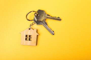 House keys with a keychain in the shape of a house.Composition on a yellow background.Design element.Real estate and insurance concept.Copy space.