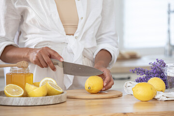 Young woman cutting lemon on wooden board. Preparation of fresh llemonade.