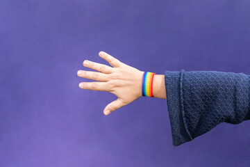 Detail of arm and hand of woman wearing gay wristband on purple background