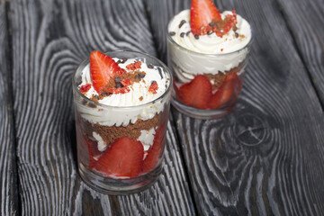 Dessert of strawberries with cream. In a glass jar. On black pine boards. Close-up.