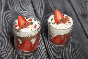 Dessert of strawberries with cream. In a glass jar. On black pine boards. Close-up.