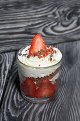 Dessert of strawberries with cream. In a glass jar. On black pine boards. Close-up.