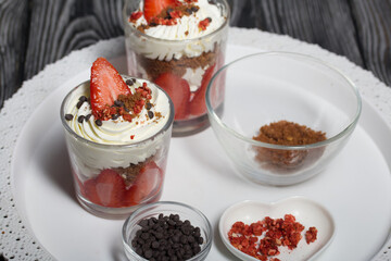 Dessert of strawberries with cream. In a glass jar. Next to the ingredients. Close-up.