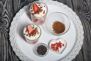 Dessert of strawberries with cream. In a glass jar. Next to the ingredients. Close-up.