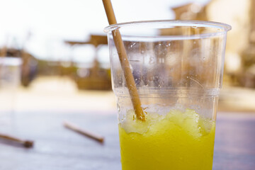 Close-up of a lemon slushie in a plastic cup, with a cardboard straw. Irony