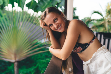 Half length portrait of cheerful female dressed in casual wear looking at camera during pastime at house balcony, happy Caucaisan woman with cute smile on face enjoying lazy sunday at terrace