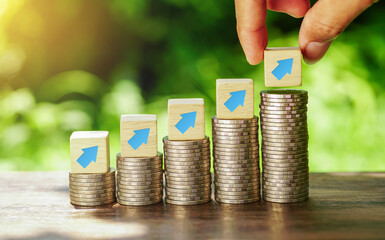 Arrow symbol on a wooden block sits on a stack of coins arranged in a ladder. with a businessman...
