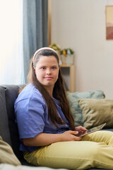 Obraz premium Cute girl with disability in casualwear using tablet at leisure while sitting on sofa in home environment and looking at camera