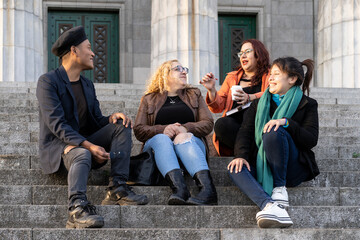 Multi ethnic group of friends sitting on some stairs having a good time chatting and laughing