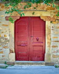 A reddish painted wooden double door and an ocher stonewall house. Campos village, Chios island, Greece.