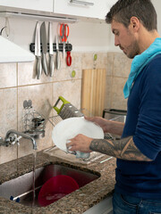 Young man with tattoo washing dishes in the kitchen