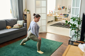 Active girl with mental disability doing stretching exercise on the floor of living room in front...