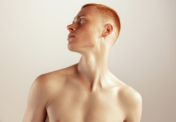 Portrait of young red-haired man posing shirtless, looking away isolated over grey studio background