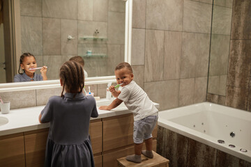 Portrait of two African American kids in bathroom focus on little toddler boy brushing teeth, copy...