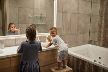 Portrait of two African American kids in bathroom focus on little toddler boy brushing teeth, copy space