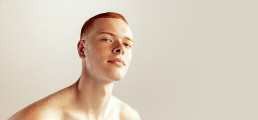 Portrait of handsome young red-haired man with freckles posing, barely smiling, looking at camera...