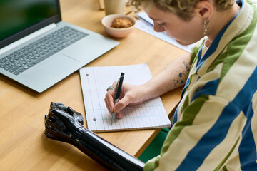 Young businesswoman with partial arm making notes or writing down working plan for week while...