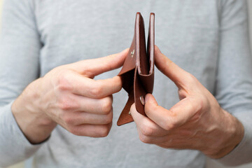 Men's hands hold an inverted empty wallet, shakes out coins from the wallet. Concept no money,...