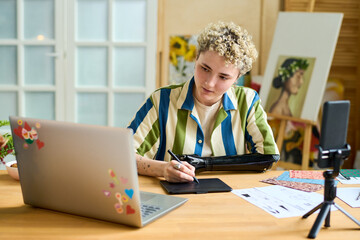 Young graphic designer and blogger with arm prosthesis creating new drawing while looking at laptop...