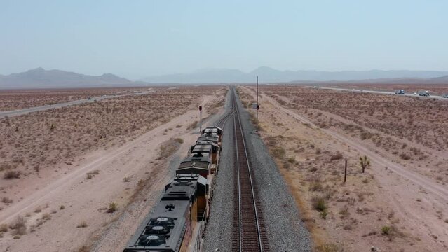 A freight train moves across the desert from a high angle. Overhead Shot of Train Engine Entering Frame from above in Aerial Drone Shot. Aerial view of freight train in desert.  USA. Drone. 4K. 