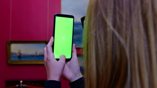 Faceless girl takes pictures of paintings she likes in museum on smartphone. Young woman visits exhibition, cultural event