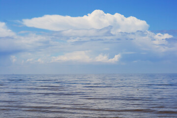 Obraz premium White clouds on blue sky over calm Baltic sea with sunlight reflection in sea. Nature shot in Latvia